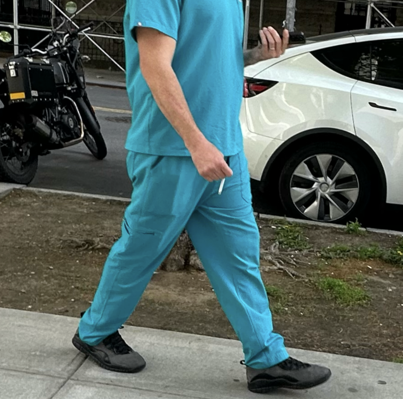 person in teal scrubs walking past a motorcycle and Tesla